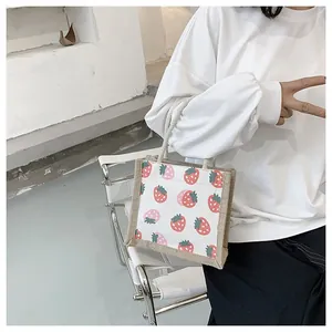 Detail of canvas tote bag featuring pink strawberry print and white rope handles