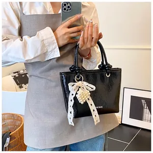 Detail of black glossy handbag with a lace bow and pearl cluster accessory