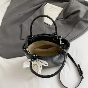 Glossy black leather crossbody handbag for women with pearl bow charm and top handle