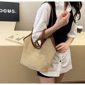 Detail of the woven straw tote bag featuring contrast dark brown leather handles