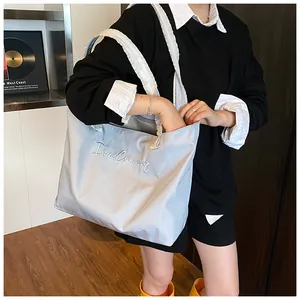 Close-up of light blue tote bag with unique ruffled strap and cursive embroidery detail