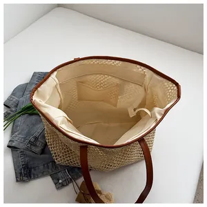 Detail view of woven straw tote bag with brown leather handles and beige fabric lining