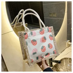 Detail of mini canvas tote bag featuring red strawberry prints and natural jute side panels