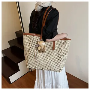 Detail of hand-woven straw tote bag with brown leather straps and cute bear charm