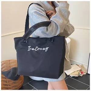 Detail of the white 'I am Creamy' embroidery on the black nylon tote bag surface