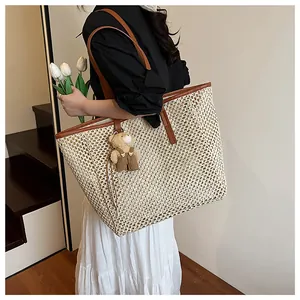 Detail of woven straw tote bag featuring brown leather handles and a cute bear charm