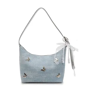 Light blue denim underarm bag with silver butterfly and pearl bow charm on white background
