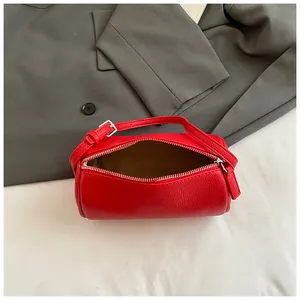 Borsa a mano cilindrica in pelle rossa testurizzata con tracolla su un blazer grigio scuro