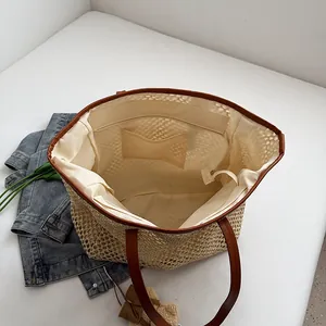 Large beige straw tote bag with brown leather handles and inner fabric pocket