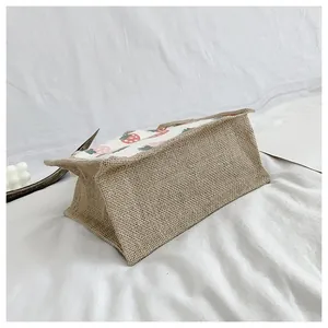 Detail shot of rectangular burlap tote bag with pink strawberry prints and textured jute