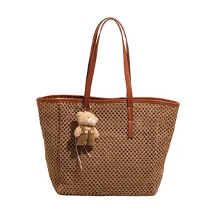 Handwoven straw tote bag with brown leather handles and a cute plush bear charm