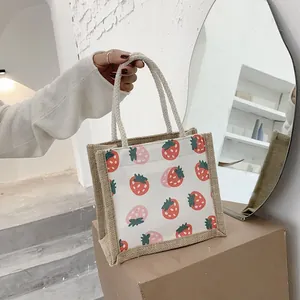Mini jute tote bag with strawberry print and rope handles on a modern display stand