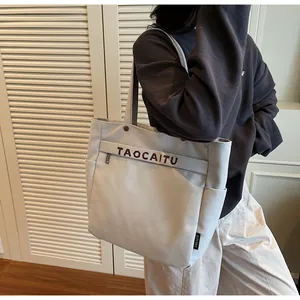 Dettaglio della grande borsa tote in tela con tasca frontale e stampa di lettere marroni