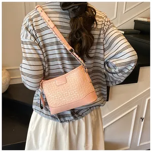 Dettaglio borsa a secchiello rosa intrecciata con tracolla a treccia indossata da modella