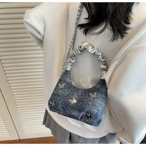 Dettaglio borsa in denim blu con farfalle metalliche argentate e tracolla a catena