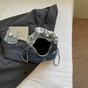 Borsa in denim blu scuro con fiocchi argentati e manico metallico su cuscino bianco