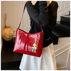 Detail of red glossy tote bag featuring a cute doll pendant and pearl chain accessory