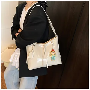 Detail of off-white patent leather shoulder bag with cute doll charm and leather tag