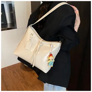 Close-up of cream white glossy leather tote bag with long straps and a cute plush charm