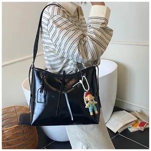 Close-up of a large black glossy tote bag featuring a cute doll charm and long straps