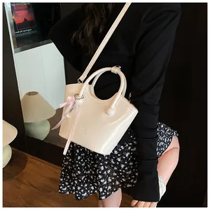 Detail of cream glossy leather tote bag with pink ribbon bow and pearl charm accent
