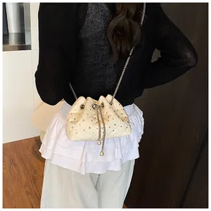 Detail of cream drawstring bucket bag with quilted rhombus pattern and crystal accents
