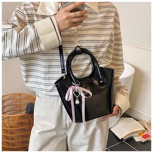 Detail of a shiny black bucket bag with pink ribbon and heart pearl charm detail