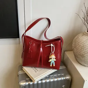Deep red glossy tote bag with leather tassels and cute doll charm on a silver suitcase