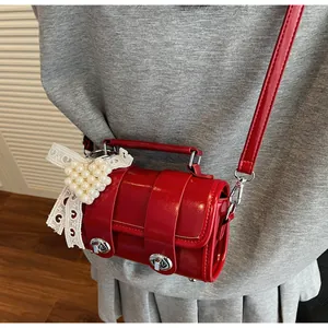 Dettaglio borsa cilindrica in pelle verniciata rossa con fibbie argento e ciondolo cuore