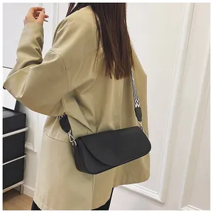 Detail view of a black rectangle crossbody bag with a patterned woven shoulder strap