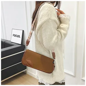 Detail of a brown crossbody bag with a leaf-shaped clasp and wavy pattern strap