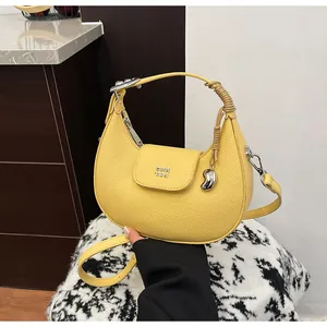 Dettaglio borsa a mezzaluna gialla in pelle con logo argento e ciondolo a chicco