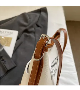 Detail of adjustable leather shoulder strap and silver buckle on canvas bucket bag