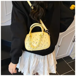 Close-up of quilted yellow bowling bag featuring silver studs and clear beaded charm chain