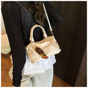 Detail of cream bowling bag with crocodile pattern and brown plush charm accessory