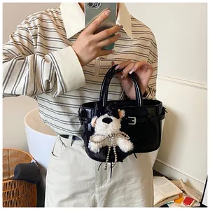 Détail du sac à main noir brillant avec boucle argentée et charmant chiot en peluche blanche