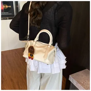 Detail of cream bowling bag featuring crocodile texture, crossbody strap and cute charm