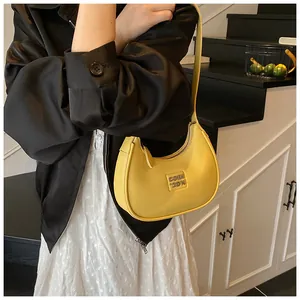 Detail view of bright yellow crescent shoulder bag with leather texture and metal logo