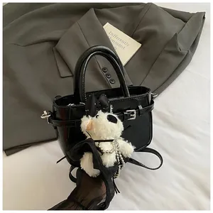 Détail d'un sac à main en cuir verni noir avec boucle de ceinture et charme de chiot