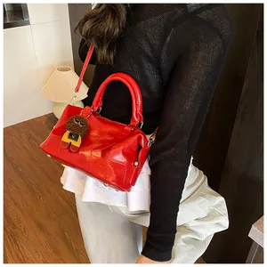 Detail of red crocodile pattern boston bag featuring a cute plush doll charm and strap