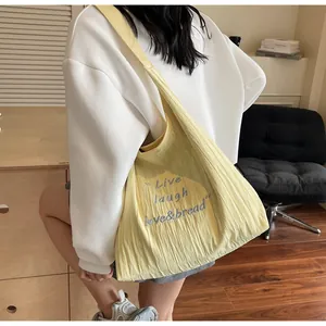 Dettaglio borsa tote gialla con ricamo 'Live laugh love' e texture in tessuto pieghettato