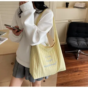Dettaglio della borsa tote gialla a pieghe con ricamo blu in un ambiente domestico caldo