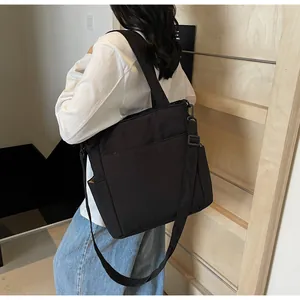 Dettaglio della borsa tote nera in tela con tasca laterale indossata da modella