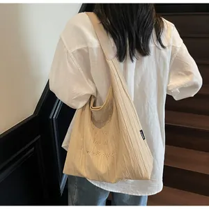 Dettaglio della borsa tote beige a pieghe con ricamo su tessuto dalla texture fine