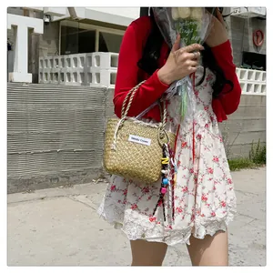 Detailed close-up of woven straw tote bag with white logo label and colorful charms