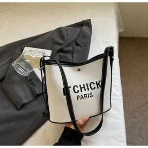 Detail of canvas bucket bag showing black leather trim and magnetic closure on white bedding