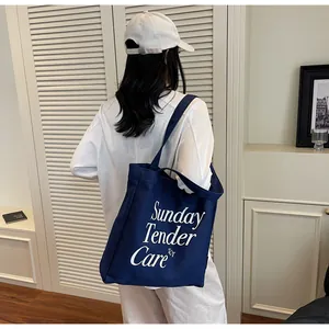 Dettaglio della borsa tote in tela blu scuro con testo Sunday Tender Care per uso quotidiano