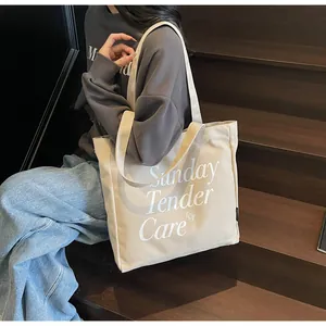 Dettaglio del testo Sunday Tender Care su borsa tote grande beige in tela con spalline