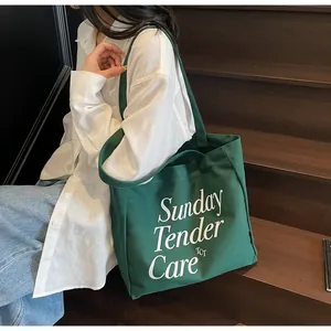 Dettaglio della borsa tote in tela verde scuro con scritte bianche e manico largo