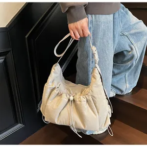 Dettaglio di una borsa a mezzaluna in nylon trapuntato beige con texture a pieghe su modella